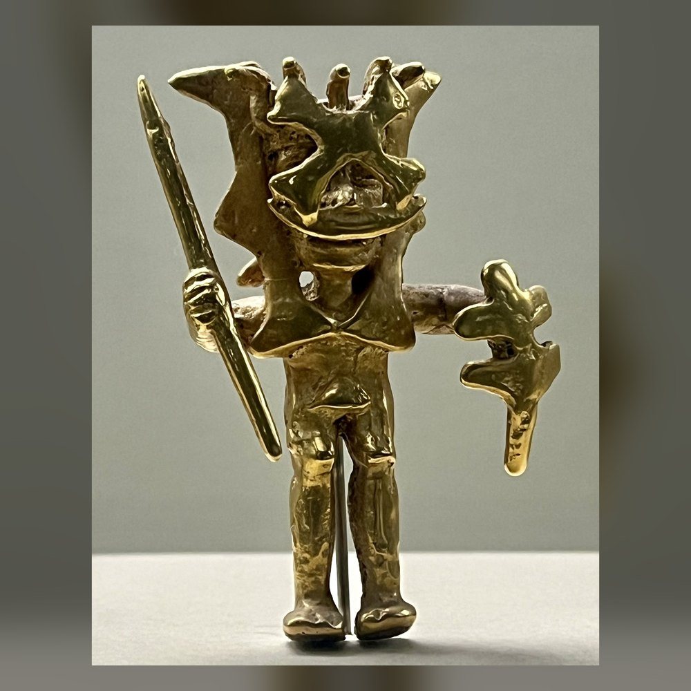 Figura de oro con tocado, bastón y un objeto en cada mano
