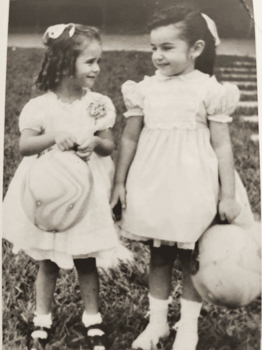 Dos niñas con vestidos claros y una pelota, sobre el pasto