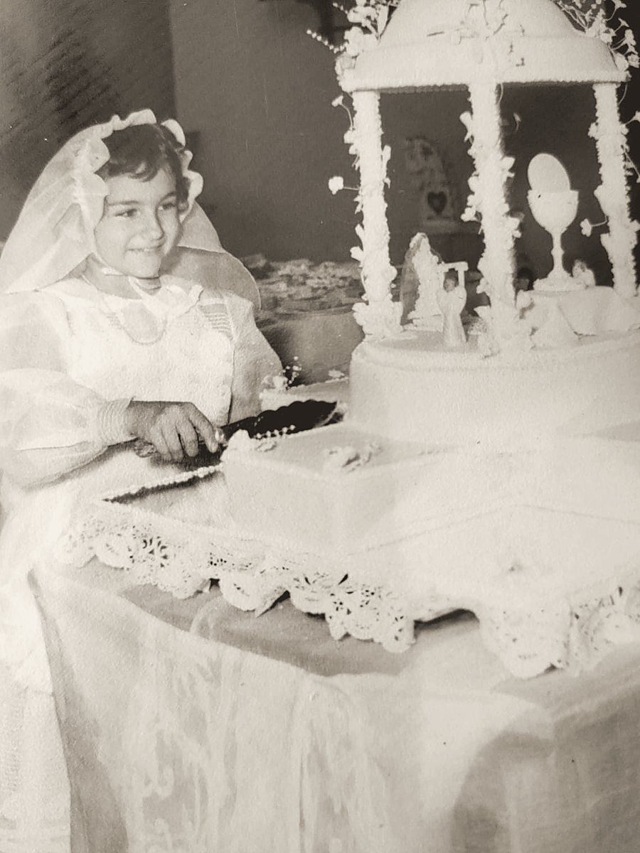 Una niña vestida de primera comunión parte un ponqué blanco