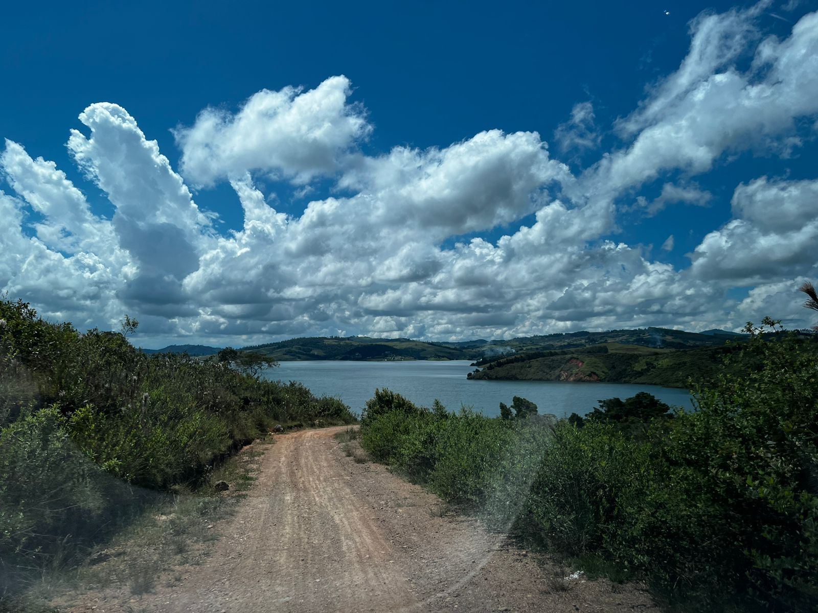 Un camino de tierra que baja hacia el lago, bajo nubes grandes