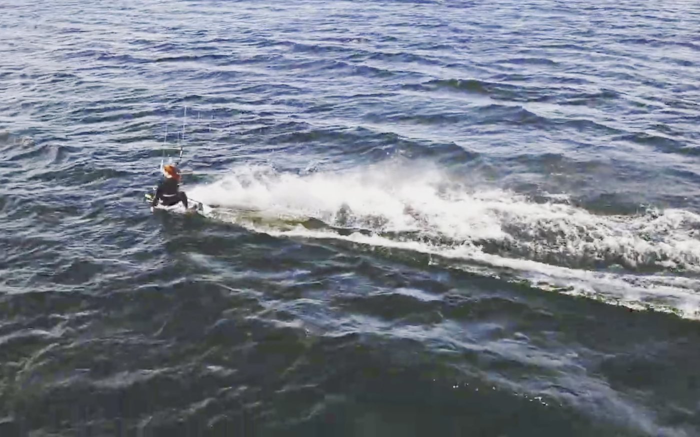 Un kitesurfista visto desde arriba gira y levanta un abanico de agua