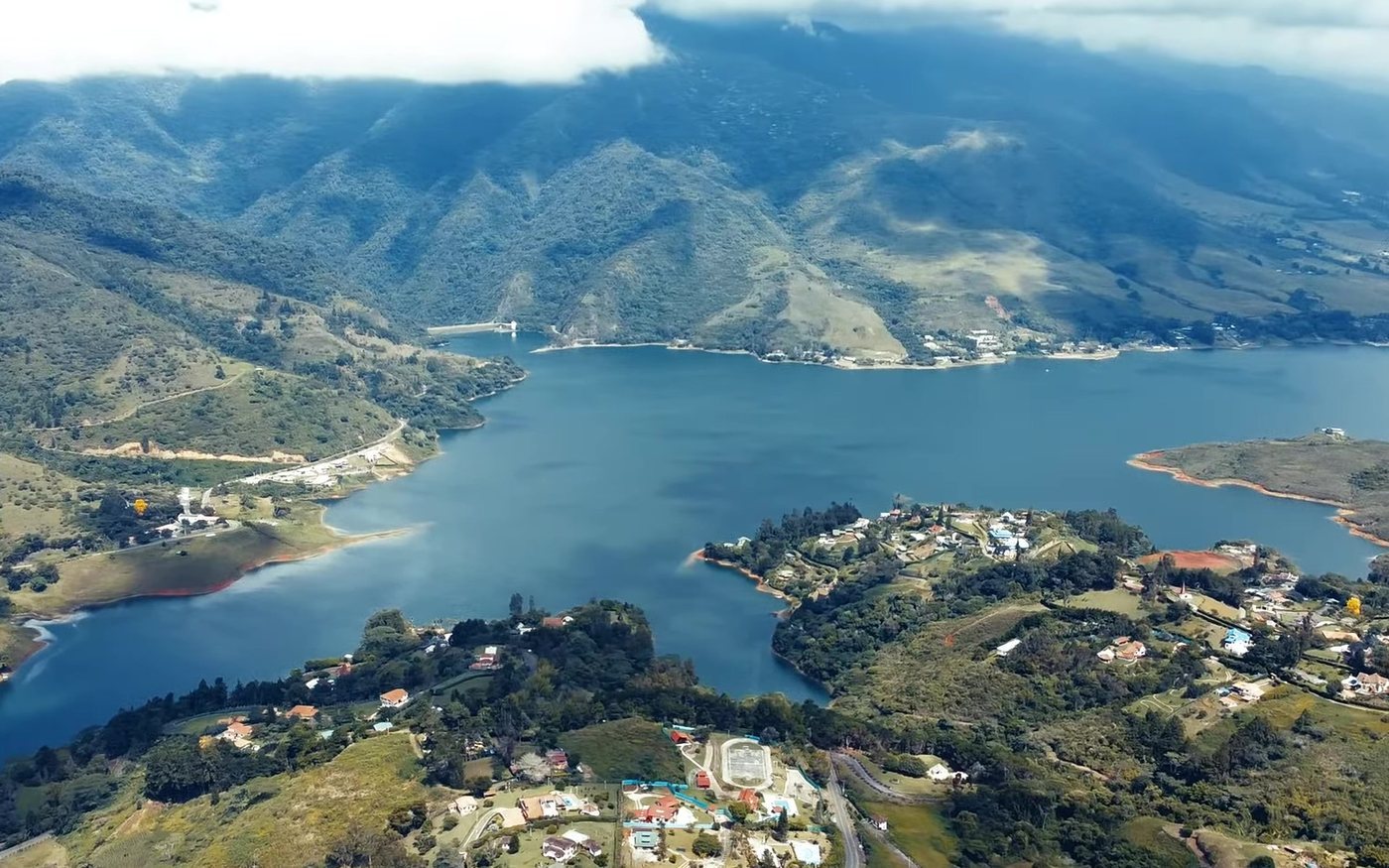 El Lago Calima visto desde un dron a lo largo, con sus brazos, casas en la orilla y montañas con nubes