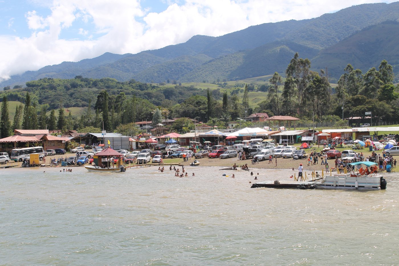 Una playa pública del Lago Calima llena de carros, carpas, quioscos y bañistas