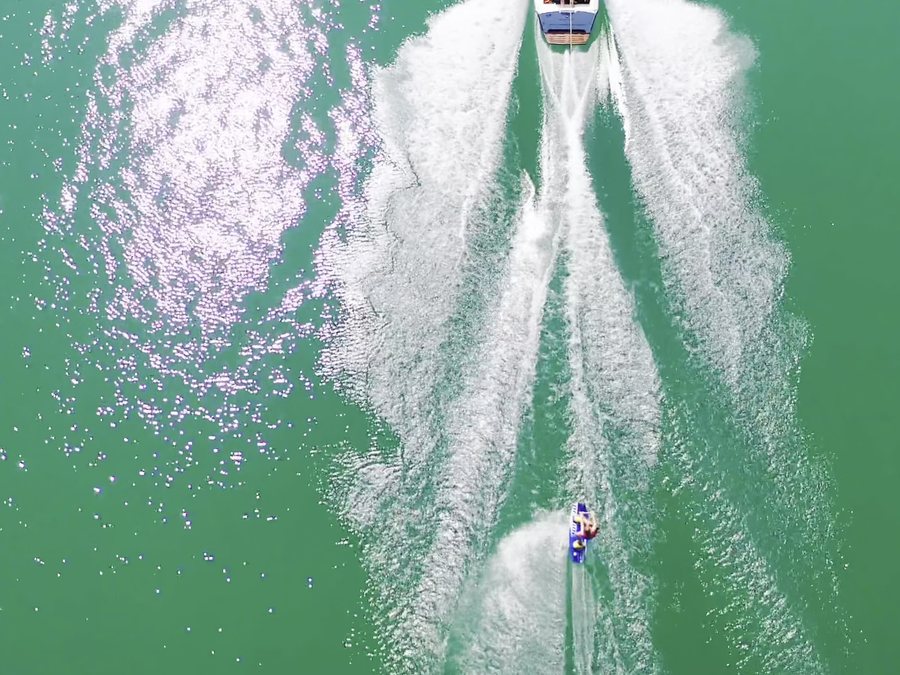 Un wakeboarder visto desde arriba, remolcado por una lancha sobre agua verde