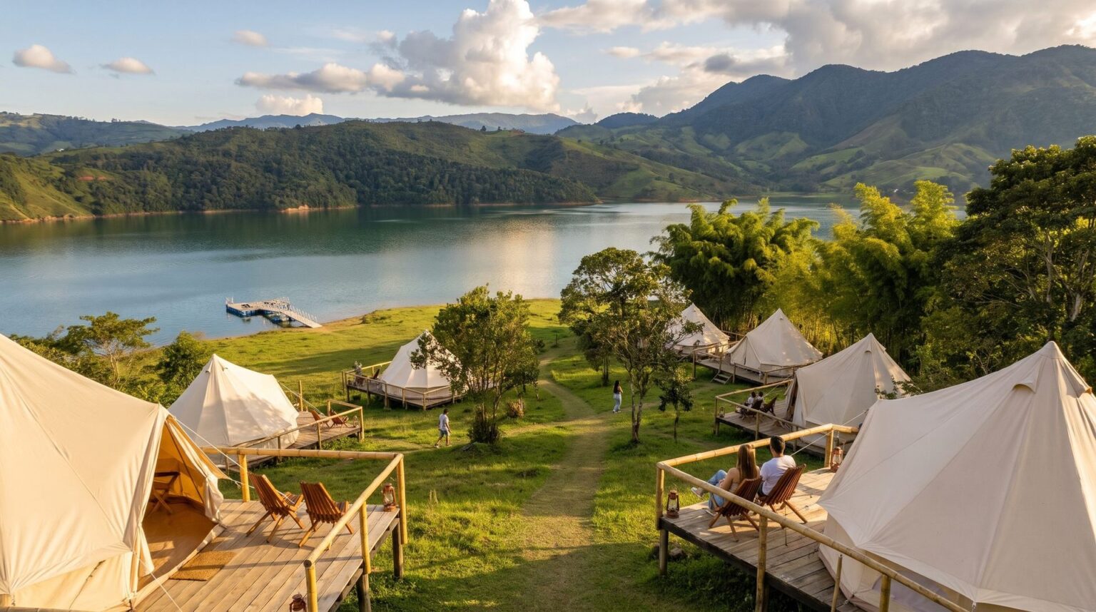 Canvas glamping tents on timber decks, widely spaced among native trees on the slope above Lake Calima, at golden hour.