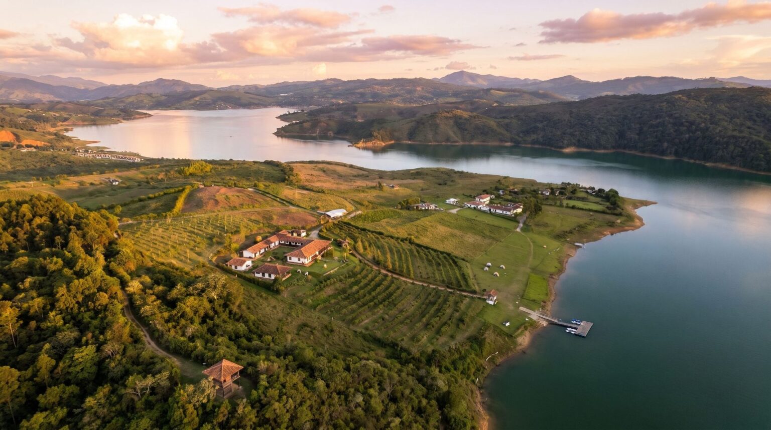Aerial view at sunset of the whole estate, from the mountain forest down to Lake Calima, with the farm and orchard on the slope and the campground by the water barely visible.