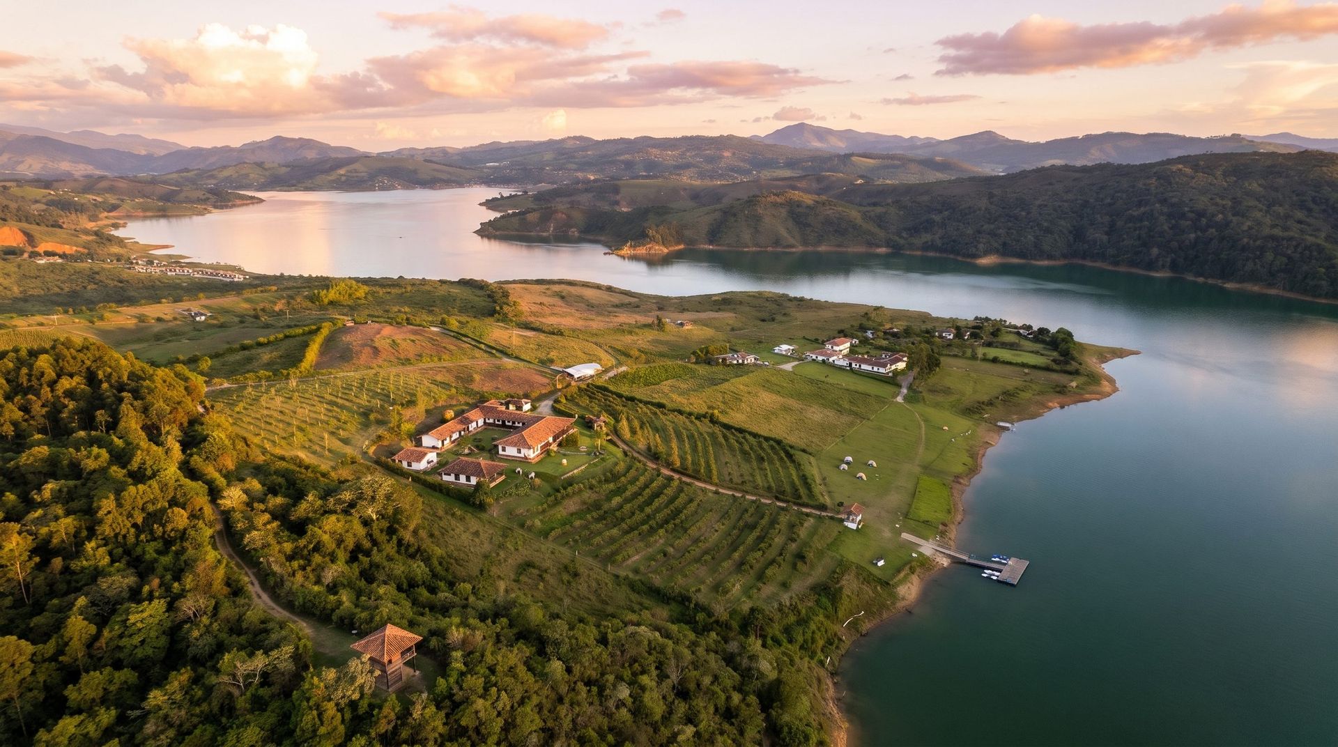 Aerial view at sunset of the whole estate, from the mountain forest down to Lake Calima, with the farm and orchard on the slope and the campground by the water barely visible.